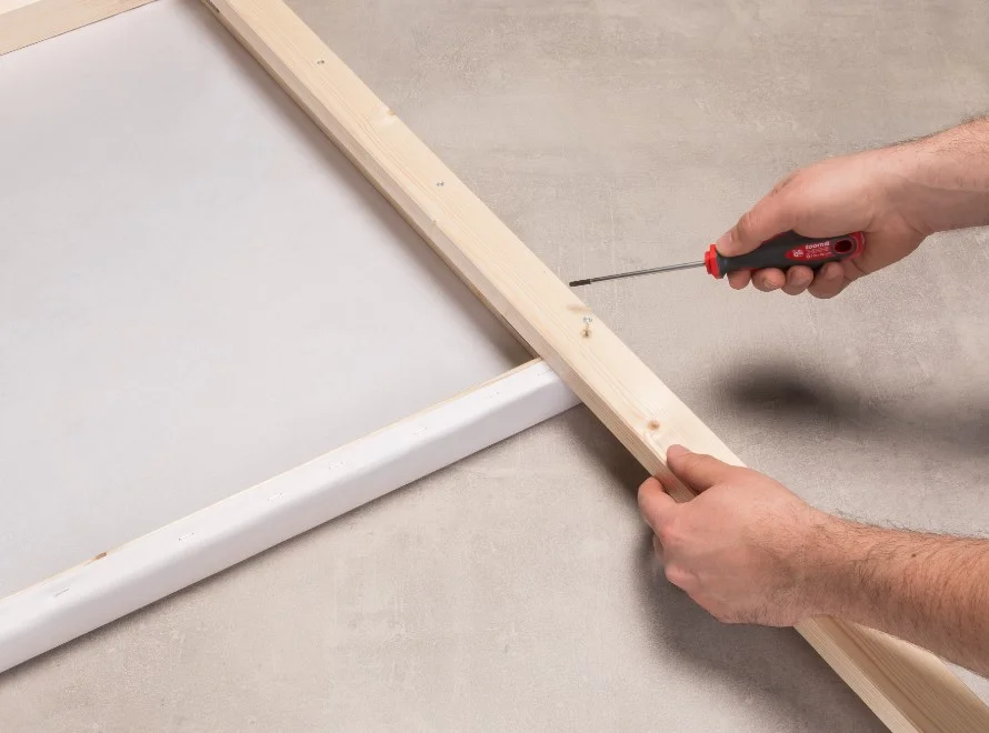 Person schraubt Leinwand auf Keilrahmen