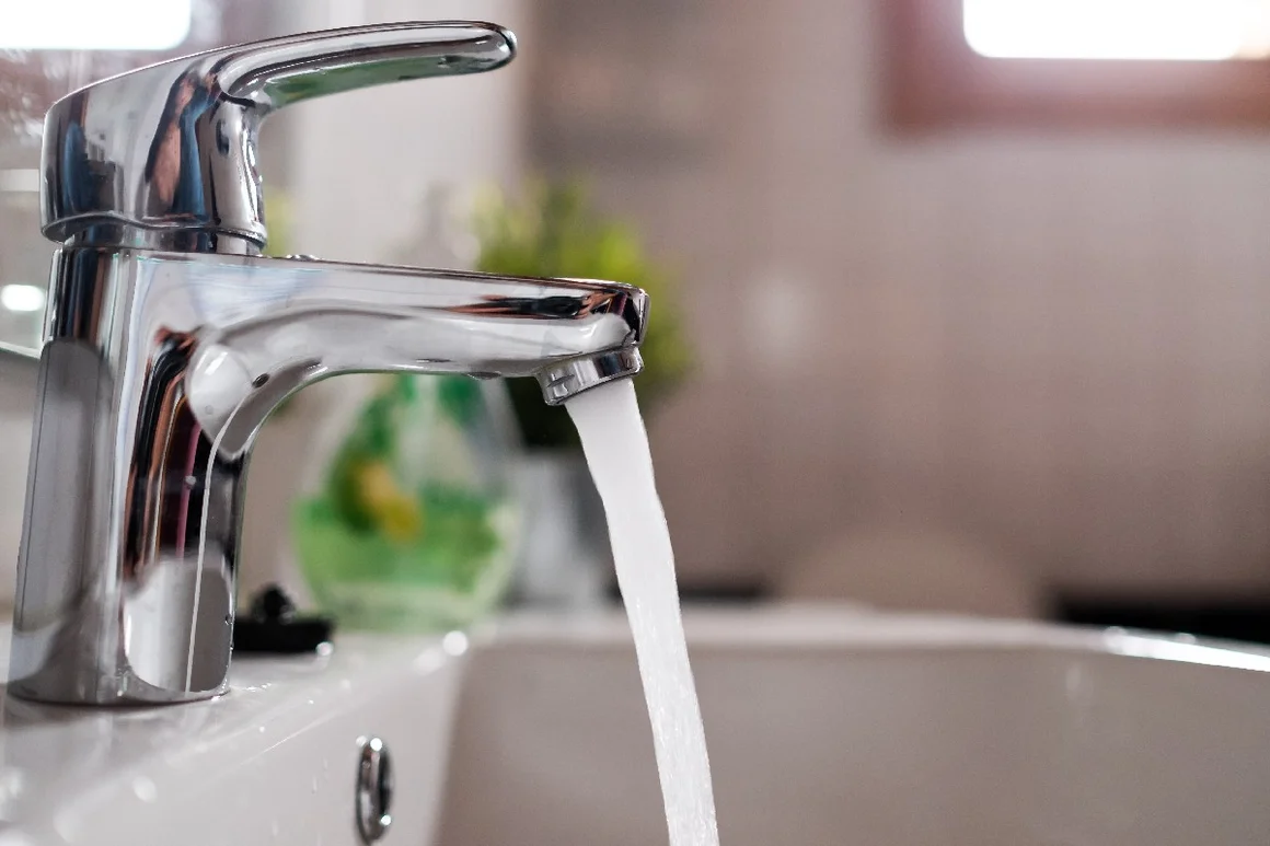 Ein Wasserstrahl läuft aus einem Wasserhahn in ein Waschbecken