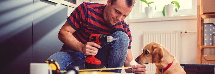 Eine Person mit einem Elektrowerkzeug in Aktion und ein Hund schaut zu