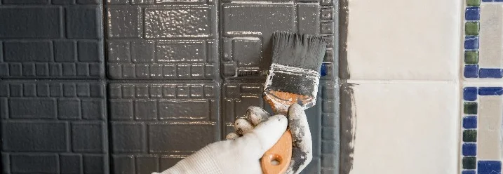 Hand trägt graue Farbe auf Fliesen auf