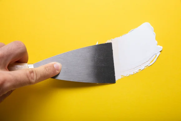 Hand verspachtelt weiße Paste auf gelbem Grund