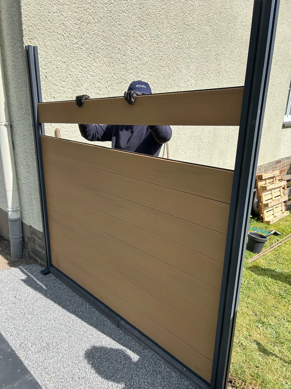 Eine Person montiert einen Sichtschutzzaun mit Lamellen in Holzoptik.