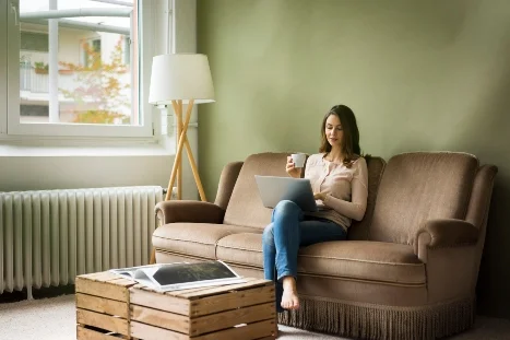 Person mit Laptop und Tasse auf Sofa