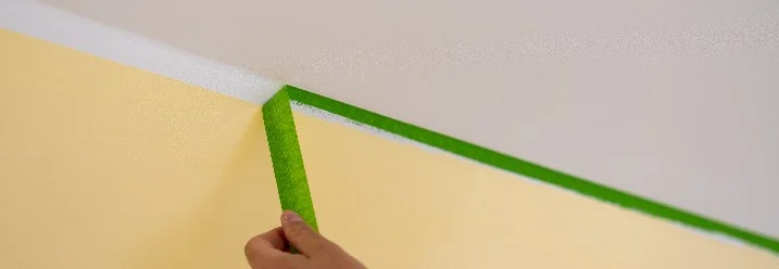 Eine Person löst Malerband von der Wand ab