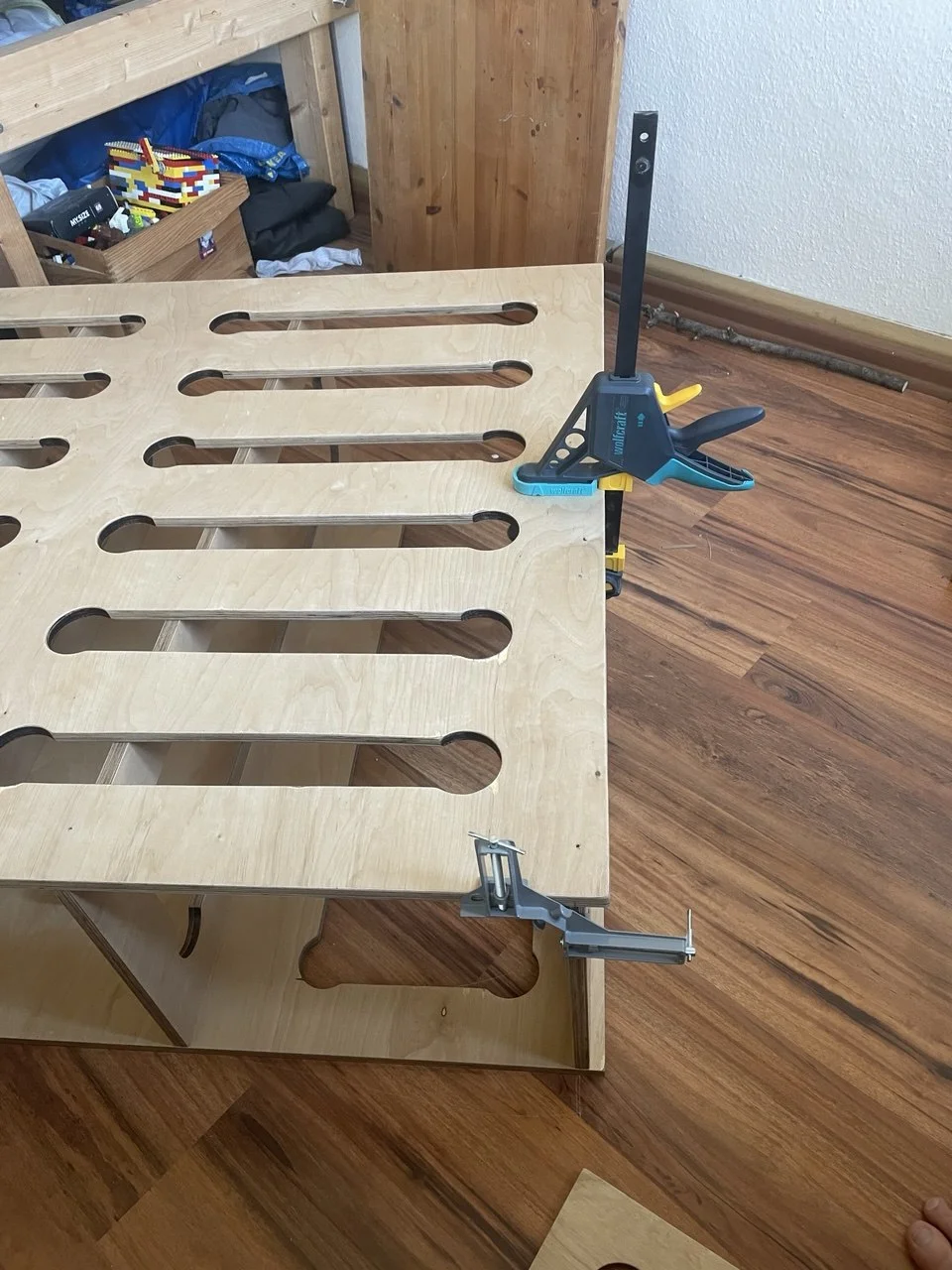 Eine Holzkonstruktion wird mit zwei Schraubzwingen auf einem Holzboden fixiert.
