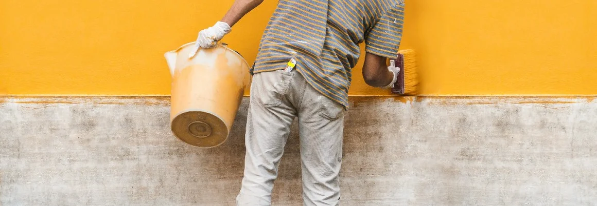 Person streicht Wand mit Pinsel gelb an