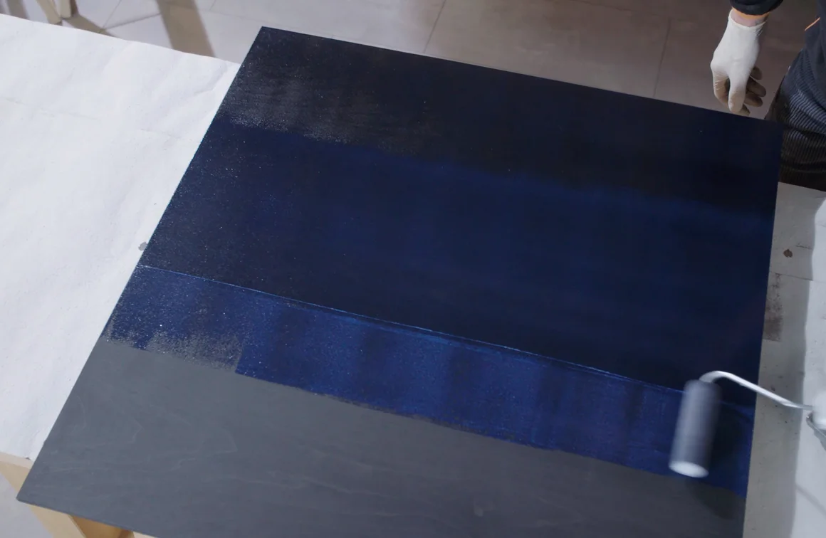 Person streicht Holzplatte mit Farbroller blau