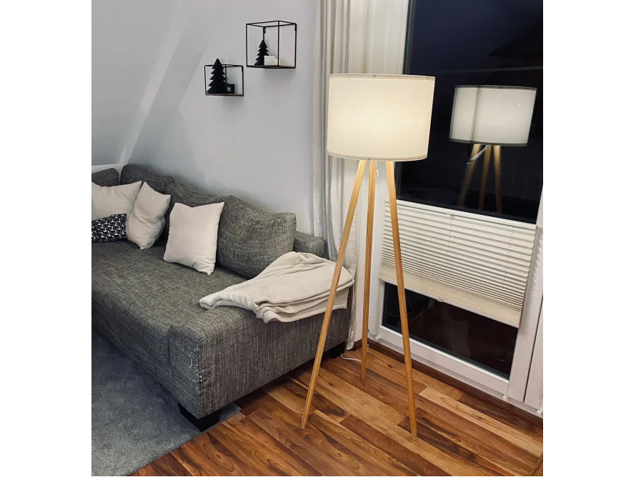 Eine Stehlampe mit Holzbeinen und weißem Lampenschirm.