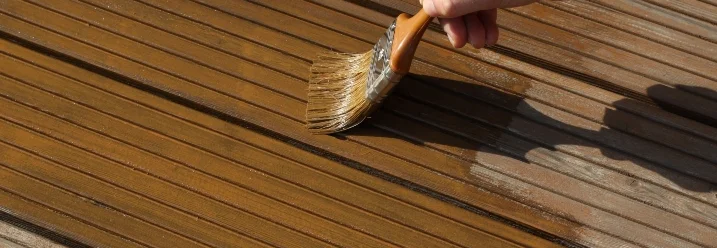 Person streicht Holzboden mit Pinsel