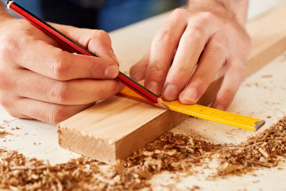 Person misst Holz mit Zollstock und Bleistift ab