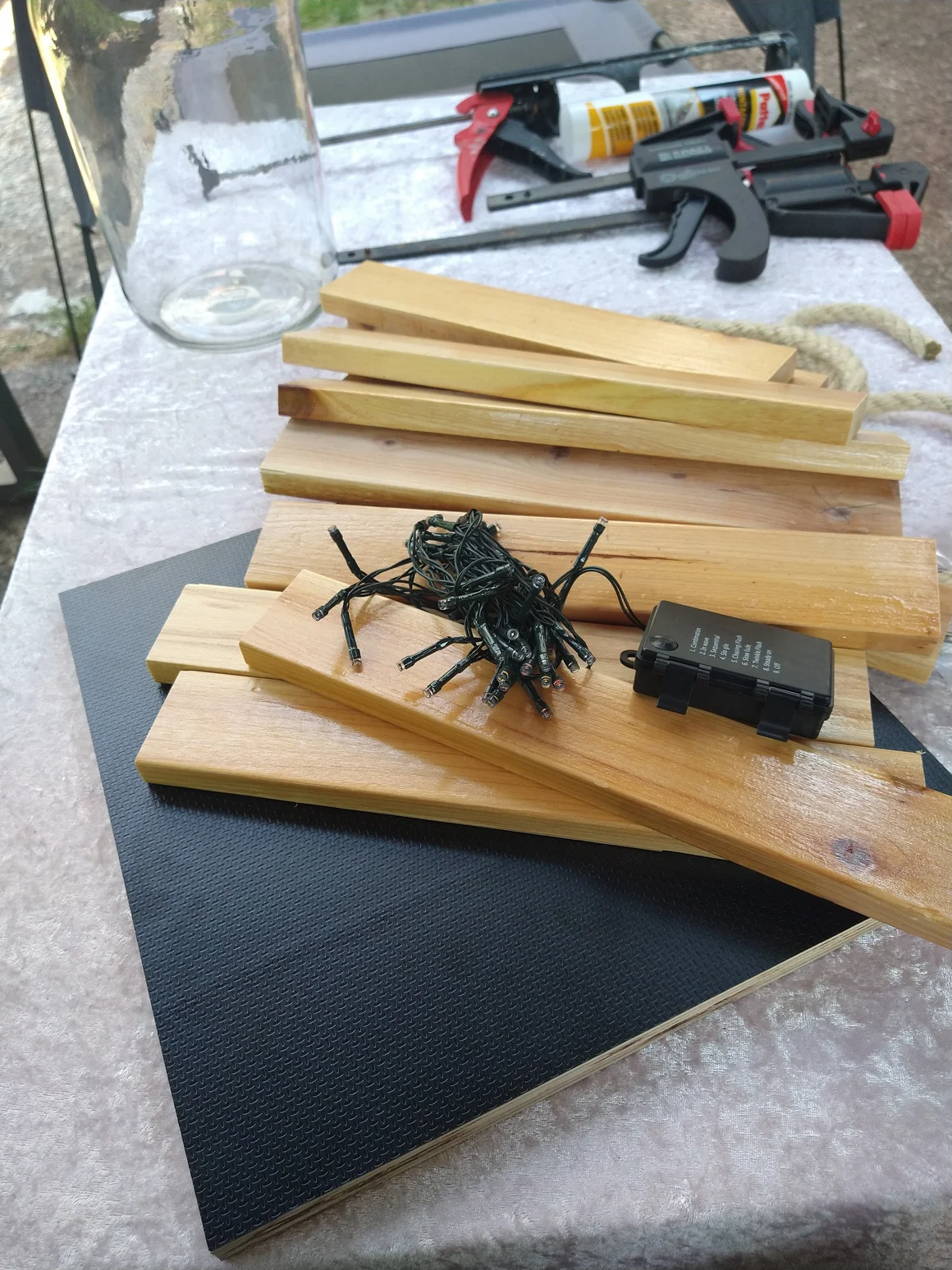 Bastelzubehör mit Holzlatten, einer Lichterkette und Schraubzwingen auf einem Tisch.