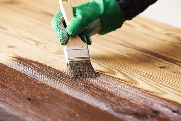 Hand in grünem Handschuh streicht Holz braun