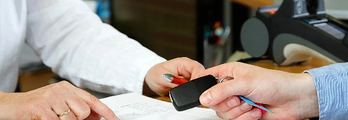 Person gibt Autoschlüssel und unterschreibt Vertrag