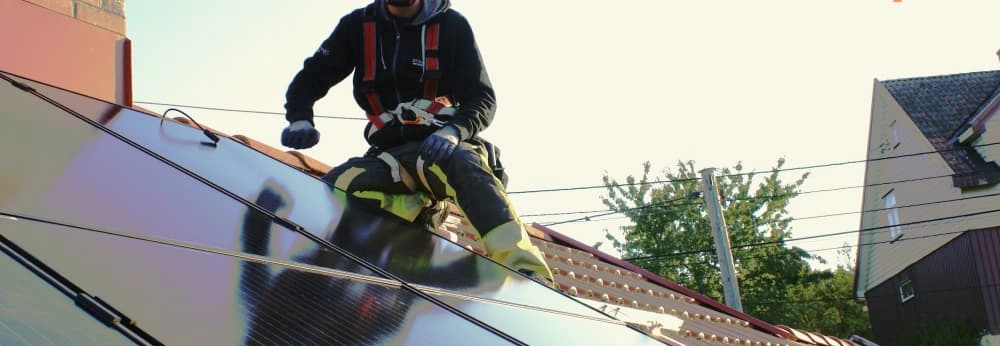 Person auf Dach installiert Solarmodule. Das Logo der Marke otovo ist abgebildet