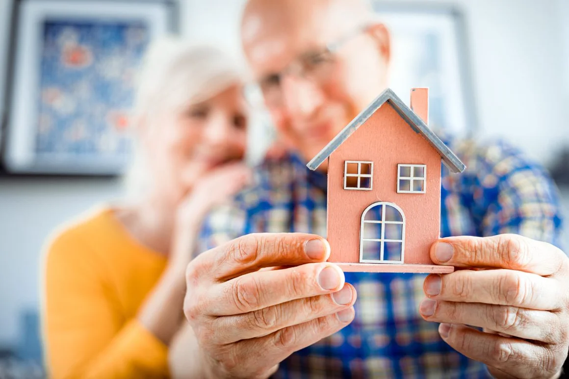 Ältere Menschen halten ein Modellhaus in den Händen.
