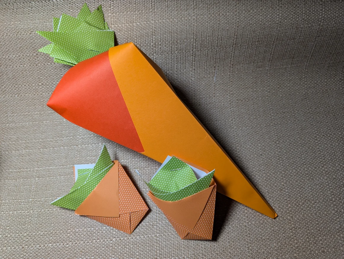 Eine große und zwei kleine Origami-Karotten aus buntem Papier.