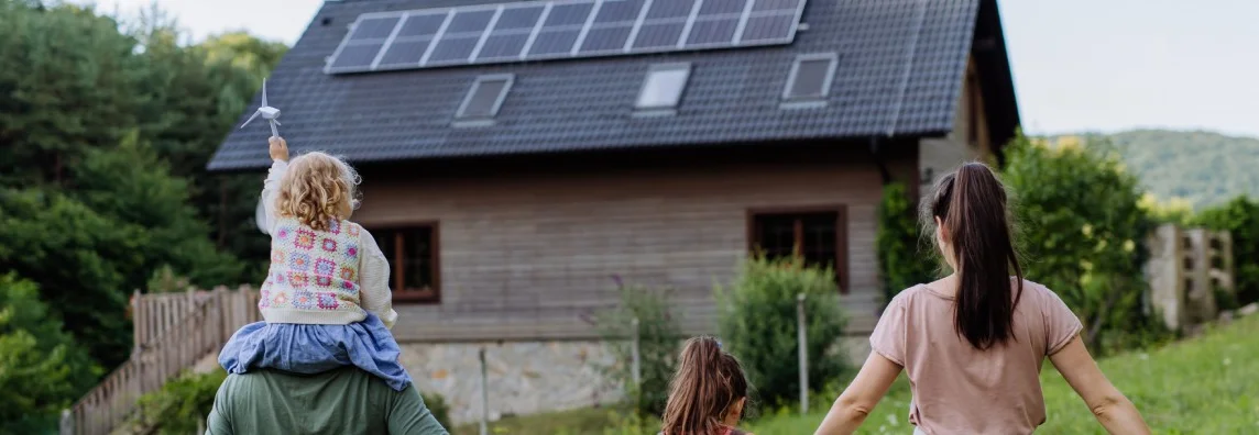 Rückansicht einer Familie, die auf ein Haus mit Solaranlage zugeht.