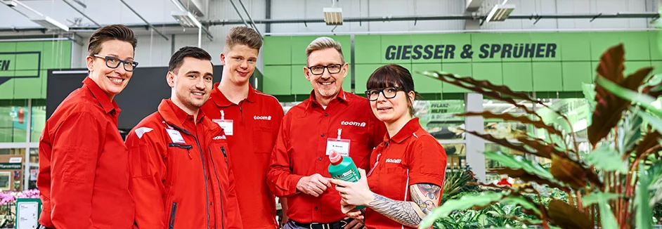 Fünf Personen in roten Arbeitsjacken von toom vor Gartenpflanzen