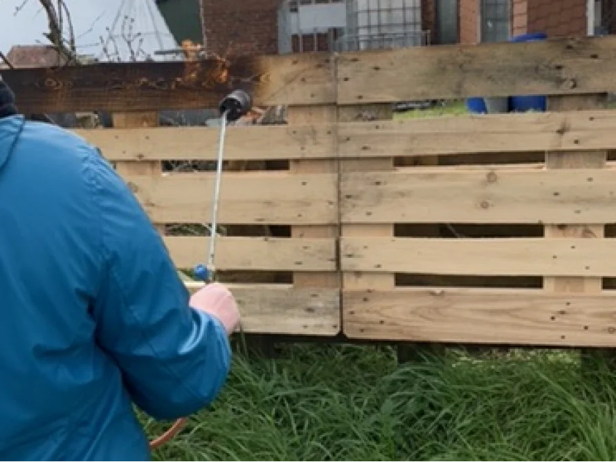 Person bearbeitet Holzlatten mit Gasbrenner