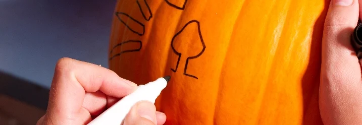 Person zeichnet mit Stift auf Kürbis