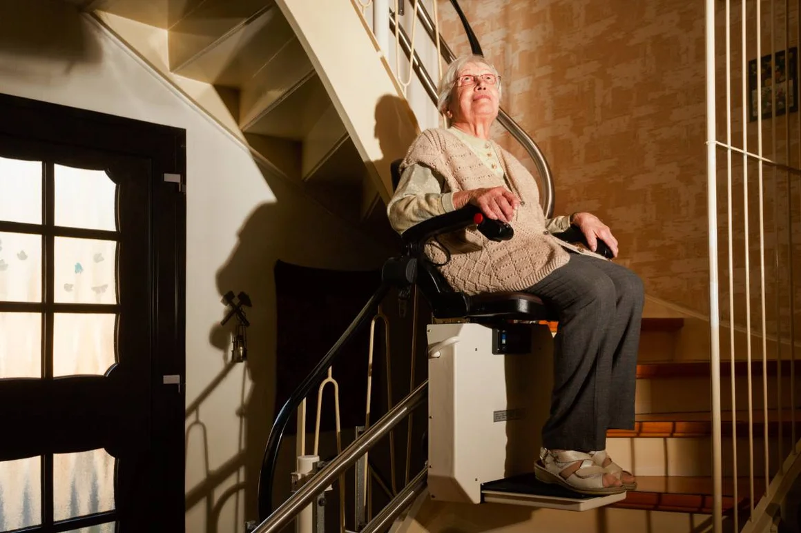 Eine ältere Person fährt in einem Treppenlift eine Treppe hinauf.