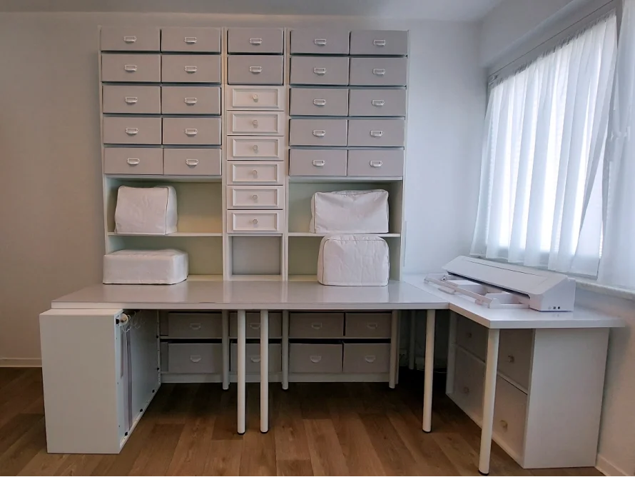 Ein Nähzimmer mit einem großen weißen Tisch und vielen Schubladen.