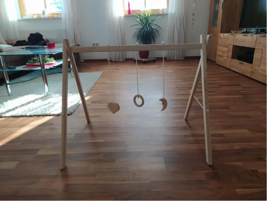 Ein hölzernes Baby-Spieltrapez mit drei hängenden Spielzeugen.