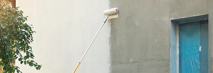Person streicht Hauswand mit Farbrolle.