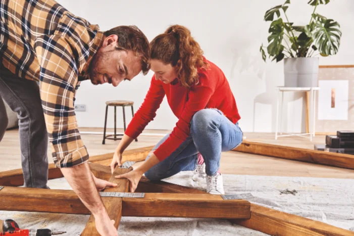 Zwei Personen bauen ein Holzgerüst mit einem Winkel zusammen.