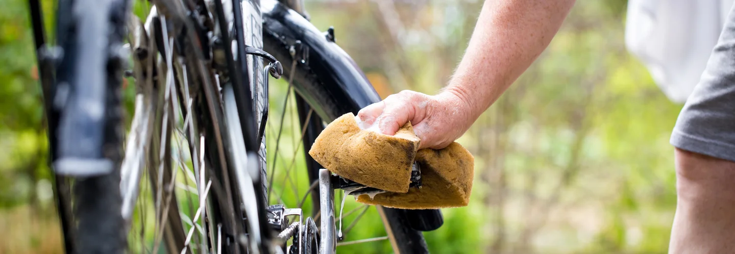 Hand mit Schwamm reinigt ein schwarzes Fahrrad.
