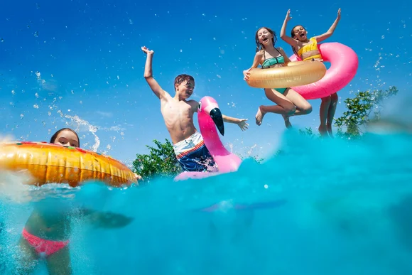 Kinder springen mit Schwimmtieren in Pool