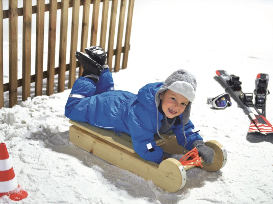 Kind liegt auf einem Holzschlitten im Schnee