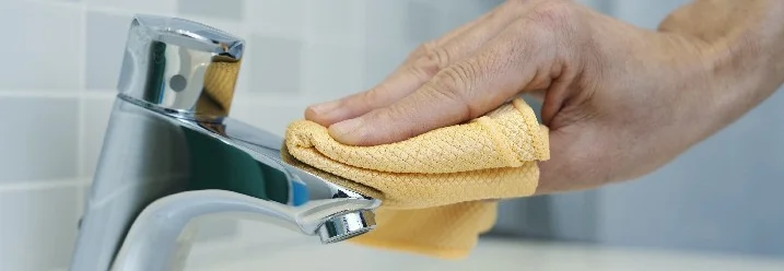 Hand reinigt Wasserhahn mit Tuch