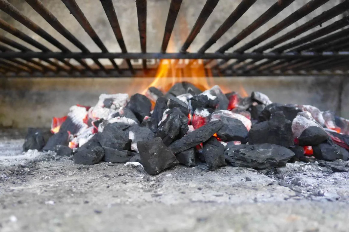 Nahaufnahme von glühender Holzkohle mit Flammen unter einem Grillrost.