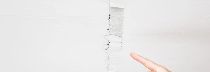 Finger zeigt auf Riss in weißer Wand