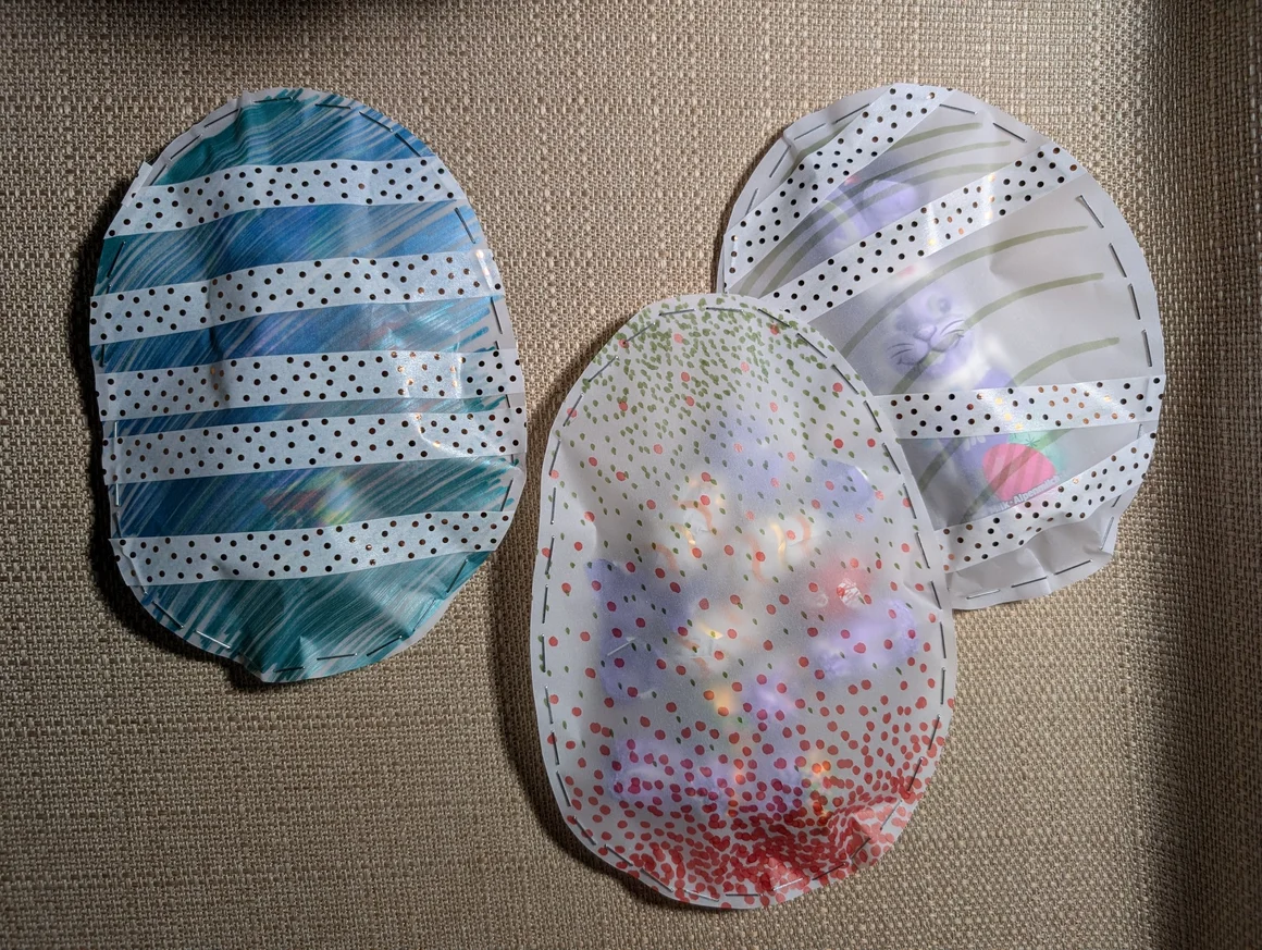 Drei selbstgebastelte Ostereier aus Transparentpapier, verziert mit gepunktetem Klebeband und zusammengeheftet.