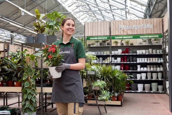 Eine toom Mitarbeiterin hält eine Pflanze in der toom Gartenwelt