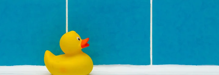 Eine gelbe Quietscheente auf dem Rand einer Badewanne.