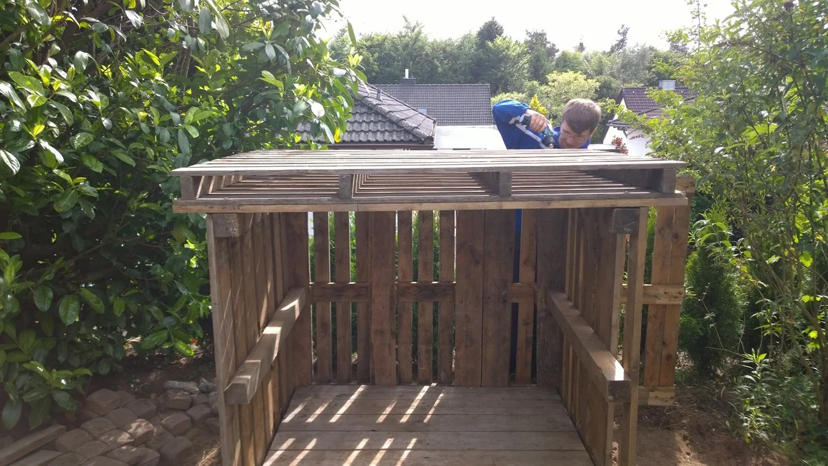 Person baut ein Gartenhaus aus Paletten.