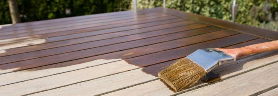Eine Holzlasur wird mit Pinsel auf Gartentisch aufgetragen