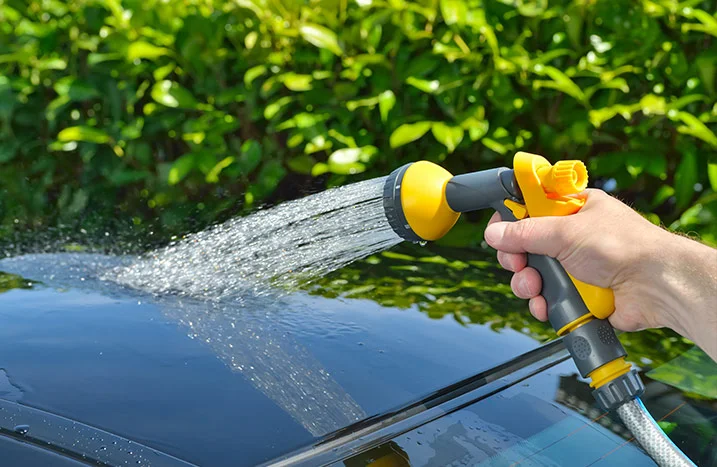 Hand spritzt Wasser auf Autodach