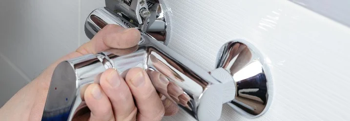 Person montiert Wasserhahn mit Schraubenschlüssel.