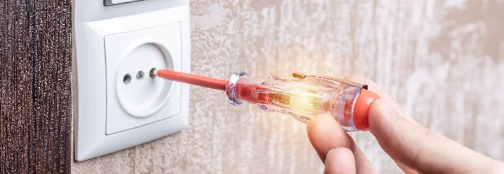 Person prüft Steckdose mit Phasenprüfer