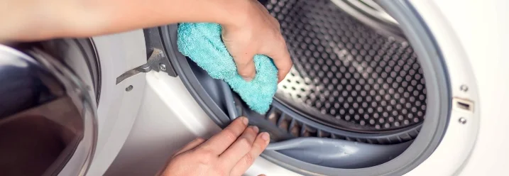 Person reinigt Waschmaschine mit Tuch