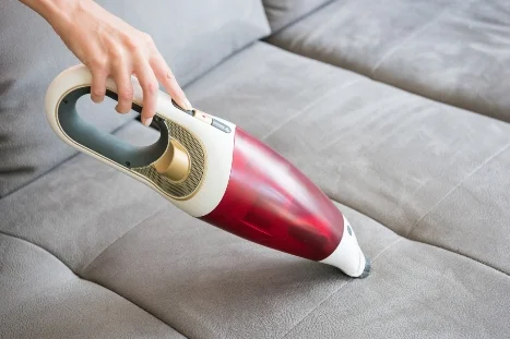 Hand saugt Sofa mit Staubsauger ab