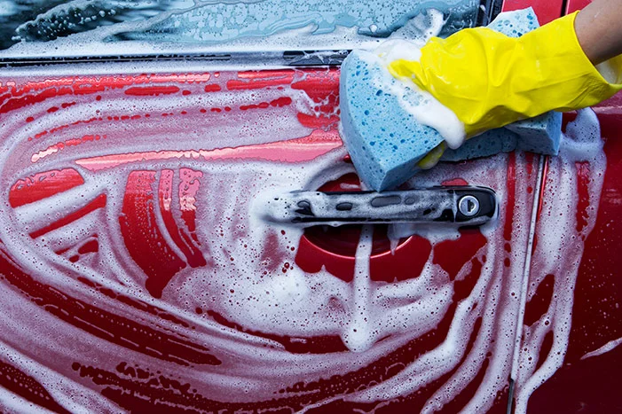 Hand wäscht rotes Auto mit Schwamm
