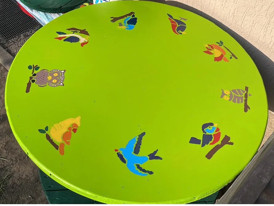 Runder grüner Tisch mit bunten Vogelmotiven