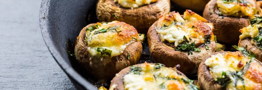 Mit Käse und Kräutern gefüllte Champignons in einer gusseisernen Pfanne.