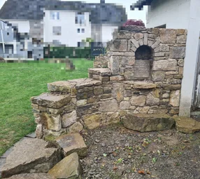 Eine aus Natursteinen gebaute Gartenmauer mit einer Nische und einer Inschrift.