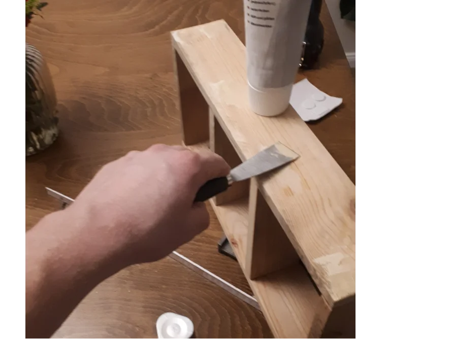 Person trägt Holzpaste mit Spachtel auf.